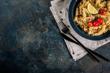 Klasik İtalyan makarna düdük pesto sos, domates, limon ve karanlık kapta taze otlar ile koyu mavi arka plan kopya alanı Üstten Görünüm