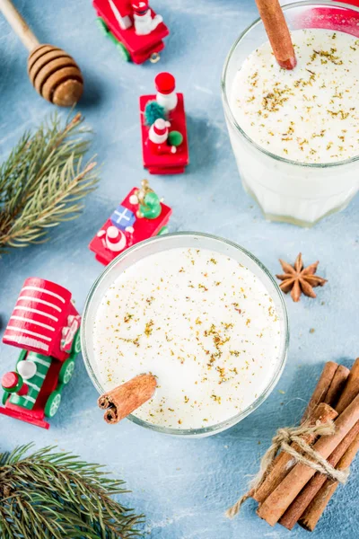 Traditional winter festive drink, sweet and spicy christmas eggnog cocktail in a glasses, on light blue background with xmas decorations, copy space top view