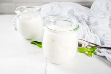 İki cam kavanoz taze ev yapımı organik yoğurt ile nane, beyaz mermer arka plan kopya alanı ile dekore edilmiştir.