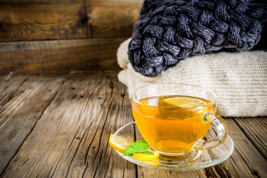 Sonbahar konfor ve sıcak kavramı. Çay cam bardağı limon, nane ve baharatlar, sıcak battaniye ile eski rustik ahşap arka plan üzerinde. Metin için yer kopyalayın