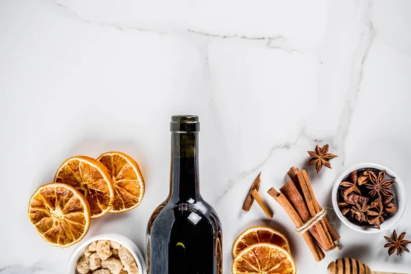 Ingredients for traditional autumn drink, mulled wine cocktail - red wine, stale oranges, cane sugar, honey, cinnamon, spices, anise, on white marble background, top view space for text