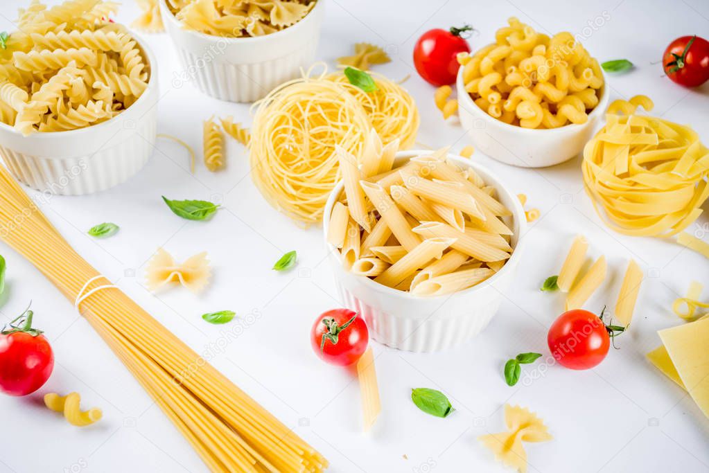 Italian food concept, various raw pasta assortment - spaghetti, lasagna, fusilli, tagliatelle, penne, tortellini, ravioli, with tomatoes and basil leaves white background copy space top view