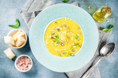 Balkabağı parmesan çorbası kabak çekirdeği, fesleğen yaprakları ve parmesan peyniri wit, mavi arka plan kopya alanı yukarıdan ışık