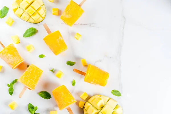 Ice cream, popsicles. Organic dietary foods, desserts. Frozen mango smoothie, with mint leaves and fresh mango fruit, on a white marble table. Copy space top view