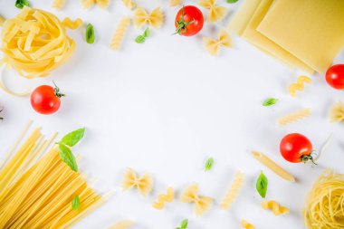 İtalyan gıda kavramı, çeşitli ham makarna çeşitler - spagetti, lazanya, düdük, tagliatelle, penne, tortellini, ravioli, domates ve fesleğen ile beyaz arka plan kopya alanı üstten görünüm bırakır