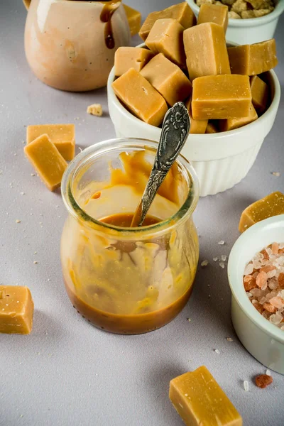 Salted caramel sauce with fudge candy, fleur de sel, brown cane sugar, grey background copy space top view