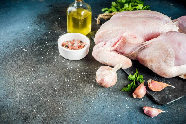 Cooking chicken background with raw whole chicken, herbs and spices, dark blue concrete table copy space top view