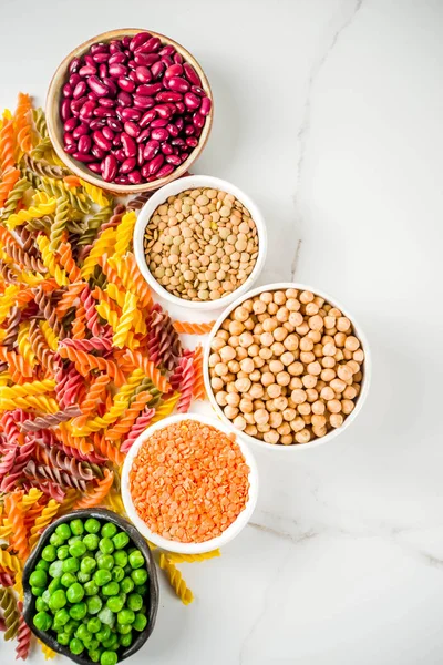 Trend healthy food, vegan diet concept. Multi colored legume pasta with raw beans. Beans, chickpeas, green peas, lentils. Copy space top view