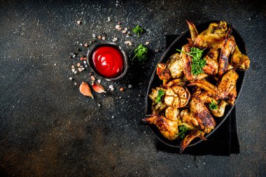 Izgara tavuk kanadı baharat ve ketçap sosu, karanlık beton zemin üzerine siyah bir plaka üzerinde pişmiş. Üstten görünüm kopya alanı