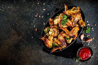 Izgara tavuk kanadı baharat ve ketçap sosu, karanlık beton zemin üzerine siyah bir plaka üzerinde pişmiş. Üstten görünüm kopya alanı