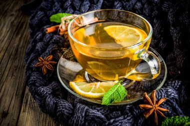 Sonbahar konfor ve sıcak kavramı. Çay cam bardağı limon, nane ve baharatlar, sıcak battaniye ile eski rustik ahşap arka plan üzerinde. Metin için yer kopyalayın