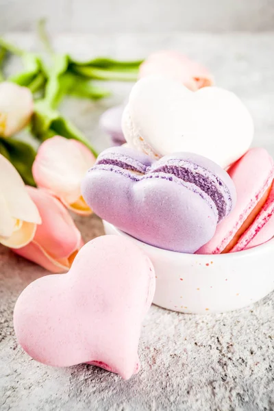 Background for greeting card Valentine's holiday. Valentine day's present, sweet treat. Homemade  pastel colored macaron cookies, with tulip flowers, on a light grey concrete background copy space