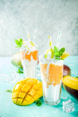 Tropikal tatlı tatlı içki. Mango milkshake ya da iki yüzlü mango dilimleri, nane ve buz küpleri, açık mavi renkli kopya alanı ile kokteyl