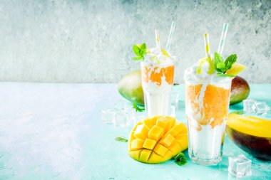 Tropikal tatlı tatlı içki. Mango milkshake ya da iki yüzlü mango dilimleri, nane ve buz küpleri, açık mavi renkli kopya alanı ile kokteyl