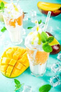 Tropikal tatlı tatlı içki. Mango milkshake ya da iki yüzlü mango dilimleri, nane ve buz küpleri, açık mavi renkli kopya alanı ile kokteyl