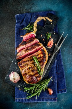 Et ve şarap ahşap kesme tahtası üzerinde çatal ile ızgara biftek dilimlenmiş. Koyu mavi arka plan. Üstten görünüm kopya alanı