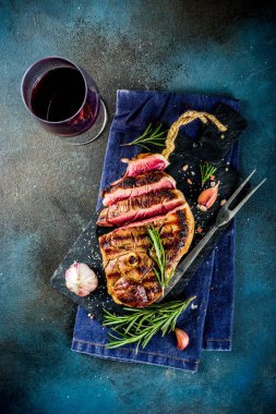 Et ve şarap ahşap kesme tahtası üzerinde çatal ile ızgara biftek dilimlenmiş. Koyu mavi arka plan. Üstten görünüm kopya alanı