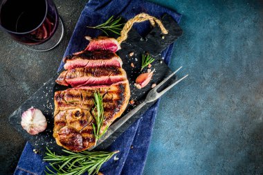 Et ve şarap ahşap kesme tahtası üzerinde çatal ile ızgara biftek dilimlenmiş. Koyu mavi arka plan. Üstten görünüm kopya alanı