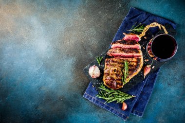 Et ve şarap ahşap kesme tahtası üzerinde çatal ile ızgara biftek dilimlenmiş. Koyu mavi arka plan. Üstten görünüm kopya alanı
