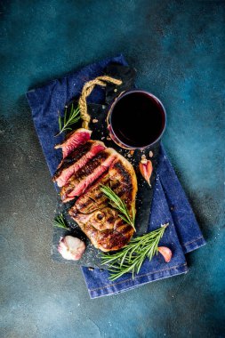 Et ve şarap ahşap kesme tahtası üzerinde çatal ile ızgara biftek dilimlenmiş. Koyu mavi arka plan. Üstten görünüm kopya alanı