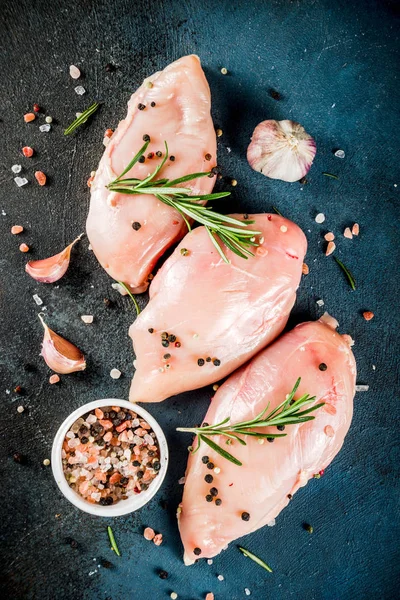 Raw fresh chicken breast fillet with spices and rosemary on a dark blue concrete background, top view with copy space for text