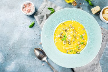 Balkabağı parmesan çorbası kabak çekirdeği, fesleğen yaprakları ve parmesan peyniri wit, mavi arka plan kopya alanı yukarıdan ışık