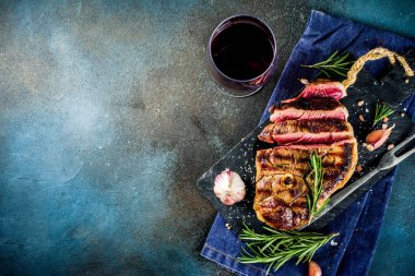 Et ve şarap ahşap kesme tahtası üzerinde çatal ile ızgara biftek dilimlenmiş. Koyu mavi arka plan. Üstten görünüm kopya alanı