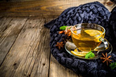 Sonbahar konfor ve sıcak kavramı. Çay cam bardağı limon, nane ve baharatlar, sıcak battaniye ile eski rustik ahşap arka plan üzerinde. Metin için yer kopyalayın