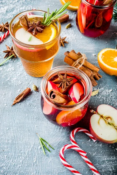 Traditional winter drinks, white and red mulled wine cocktail,  with white and red wine, spices, apple, orange. On a light blue table,