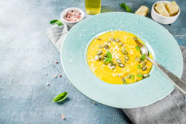 Balkabağı parmesan çorbası kabak çekirdeği, fesleğen yaprakları ve parmesan peyniri wit, mavi arka plan kopya alanı yukarıdan ışık