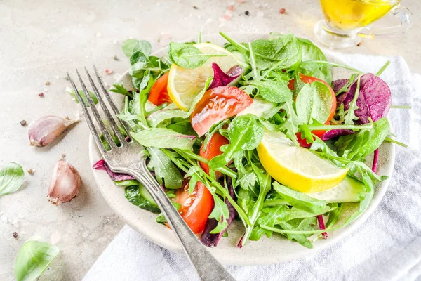 Fresh spring detox mix salad with vegetables (cucumber, lemon, tomato, arugula, and baby spinach), on light slate, stone or concrete background. Top view copy space