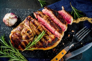 Et ve şarap ahşap kesme tahtası üzerinde çatal ile ızgara biftek dilimlenmiş. Koyu mavi arka plan. Üstten görünüm kopya alanı