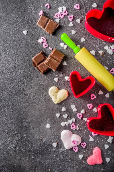 Valentine day baking concept, sweets and baking cooking background for Valentine`s day, with rolling pin, cookie cutters, sugar sprinkling, chocolate. Black concrete table top view copy space