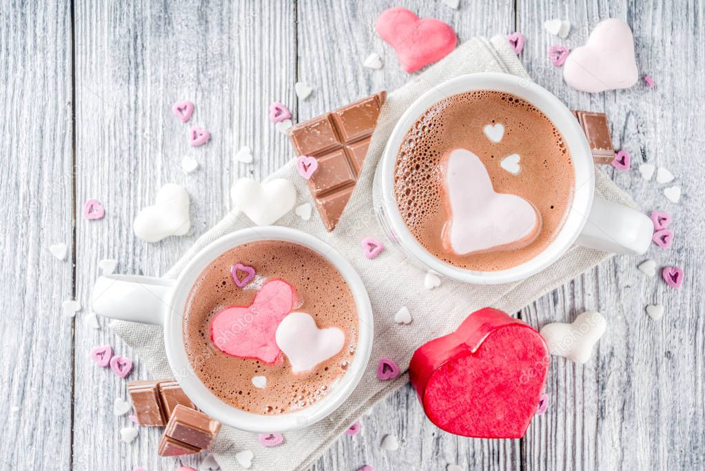 Valentines day treat ideas, two cups hot chocolate drink with marshmallow hearts red pink white color with chocolate pieces, sugar sprinkles, old wooden background copy space top view