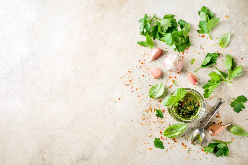 Argentinian traditional food, raw homemade green Chimichurri salsa or sauce woth parsley, garlic, basil leaves, hot pepper and spices, light stone table copy space 
