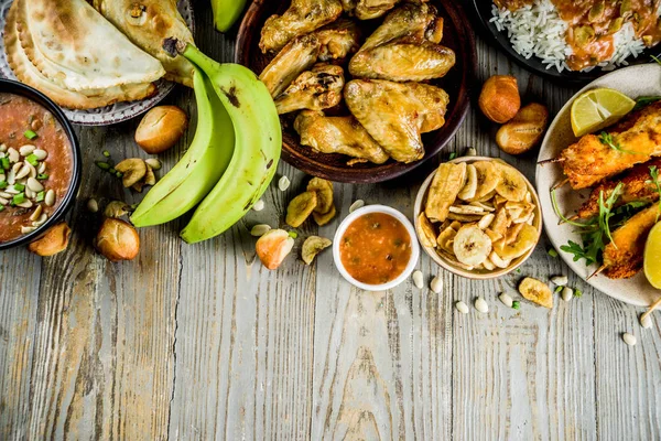 West african food concept. Traditional Wset African dishes assortment - peanut soup, jollof rice, grilled chicken wings, dry fried bananas plantains, nigerian chicken kebabs, meat pies, top view