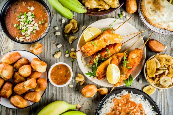 West african food concept. Traditional Wset African dishes assortment - peanut soup, jollof rice, grilled chicken wings, dry fried bananas plantains, nigerian chicken kebabs, meat pies, top view