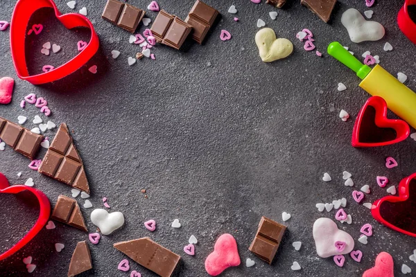 Valentine day baking concept, sweets and baking cooking background for Valentine`s day, with rolling pin, cookie cutters, sugar sprinkling, chocolate. Black concrete table top view copy space