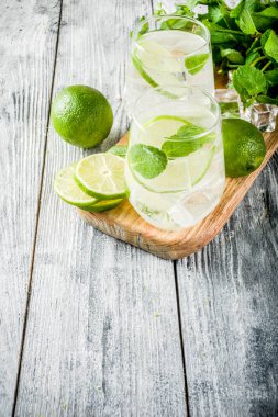 Yaz ekşi içkiyle, kireç ve buz küpleri, kopyalama alanı nane, ev yapımı kokteyl mojito ile taze limes, nane yaprağı, iki bardak, Beyaz ahşap arka plan