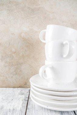 Ürün yelpazesine yığın temiz boş yeni beyaz mutfak gereçleri, tabak, kase, bardak bardak. Beyaz bir beton zemin üzerine