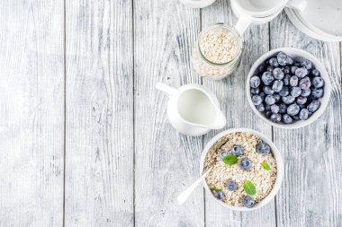 Beyaz ahşap beton arka plan kopya alanı sağlıklı tahıl ve süt kahvaltı kavramı, süt ve taze yaban mersini, küçük kase kuru yulaf
