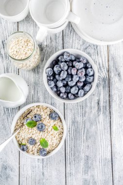 Beyaz ahşap beton arka plan kopya alanı sağlıklı tahıl ve süt kahvaltı kavramı, süt ve taze yaban mersini, küçük kase kuru yulaf