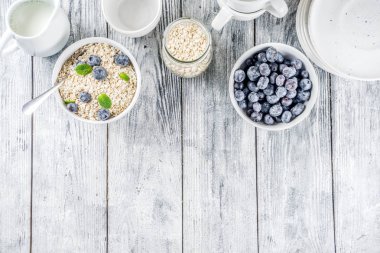 Beyaz ahşap beton arka plan kopya alanı sağlıklı tahıl ve süt kahvaltı kavramı, süt ve taze yaban mersini, küçük kase kuru yulaf