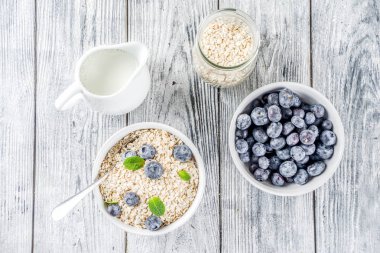 Beyaz ahşap beton arka plan kopya alanı sağlıklı tahıl ve süt kahvaltı kavramı, süt ve taze yaban mersini, küçük kase kuru yulaf