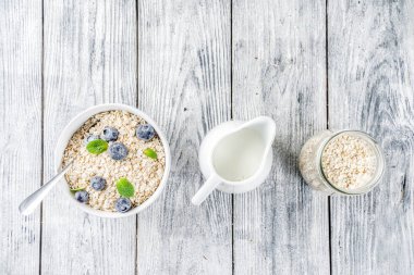 Beyaz ahşap beton arka plan kopya alanı sağlıklı tahıl ve süt kahvaltı kavramı, süt ve taze yaban mersini, küçük kase kuru yulaf