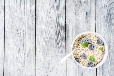 Beyaz ahşap beton arka plan kopya alanı sağlıklı tahıl ve süt kahvaltı kavramı, süt ve taze yaban mersini, küçük kase kuru yulaf