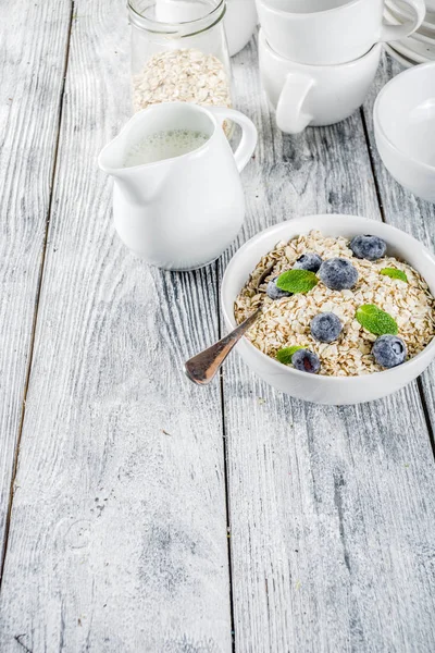 Healthy cereal and milk breakfast concept, dry oats in small bowl, with milk and fresh blueberry, white  wooden concrete background copy space