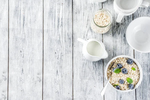 Healthy cereal and milk breakfast concept, dry oats in small bowl, with milk and fresh blueberry, white  wooden concrete background copy space