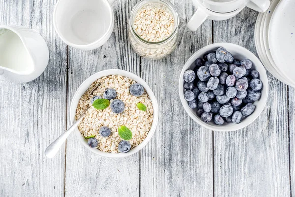 Healthy cereal and milk breakfast concept, dry oats in small bowl, with milk and fresh blueberry, white  wooden concrete background copy space