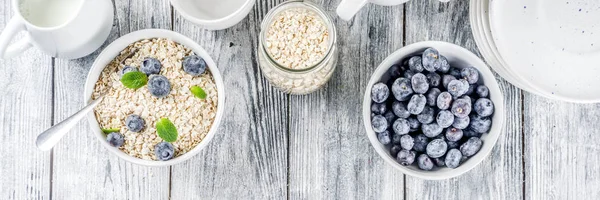 Healthy cereal and milk breakfast concept, dry oats in small bowl, with milk and fresh blueberry, white  wooden concrete background copy space banner